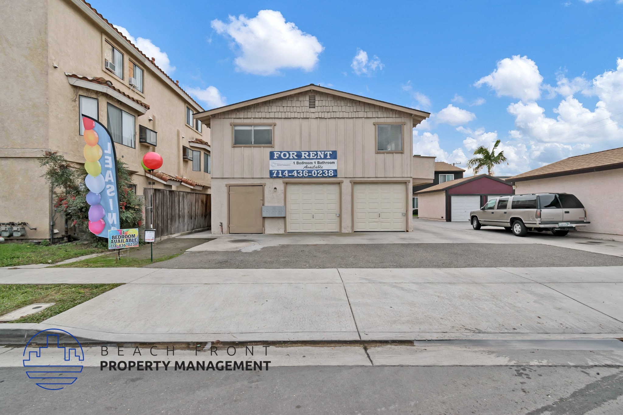 A building with a sign that says "FOR RENT" is in front of a parked car.